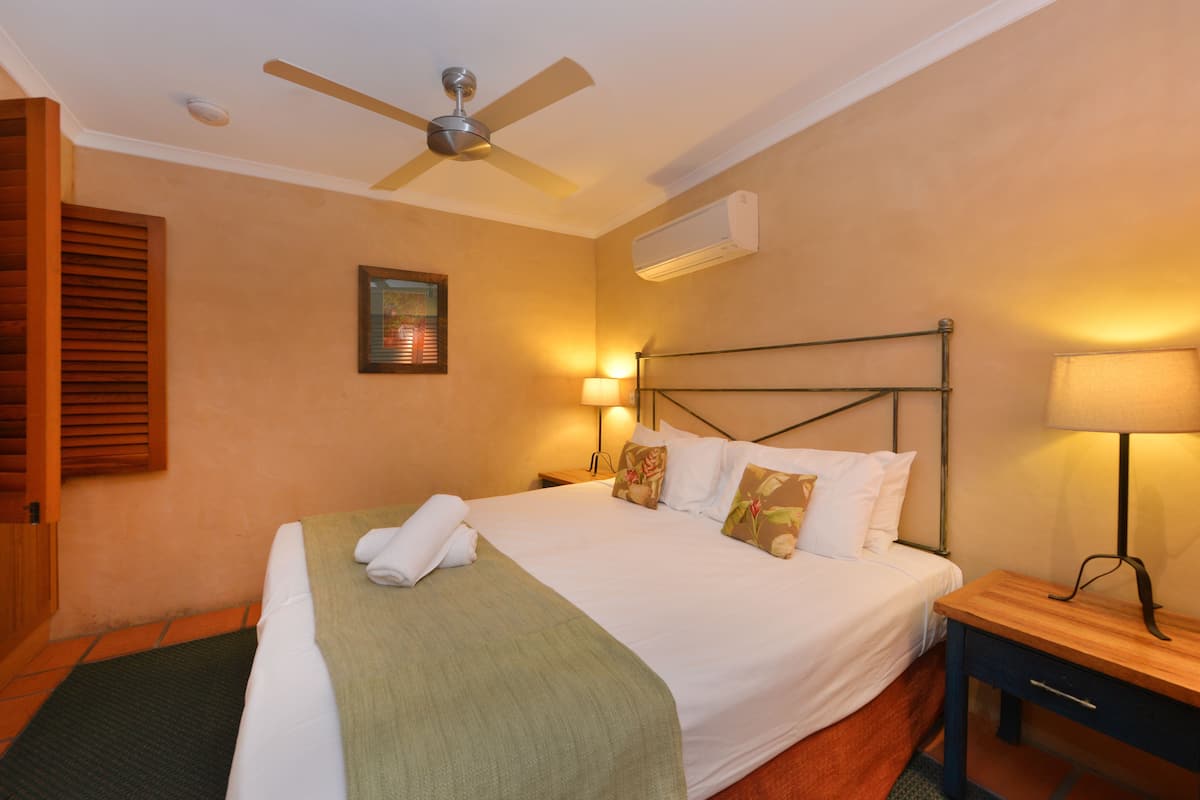 Une chambre d’hôtel équipée d’un lit, d’une table de chevet, d’un bureau, d’un ventilateur de plafond et d’un appareil de climatisation.