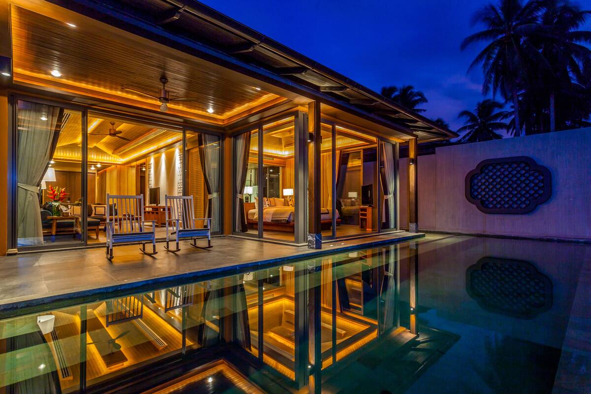 A modern hotel with a glass pool, wooden interior, and a view of palm trees.