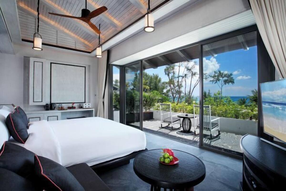A modern hotel room with a large bed, a dining area, and a balcony with a view of the ocean.