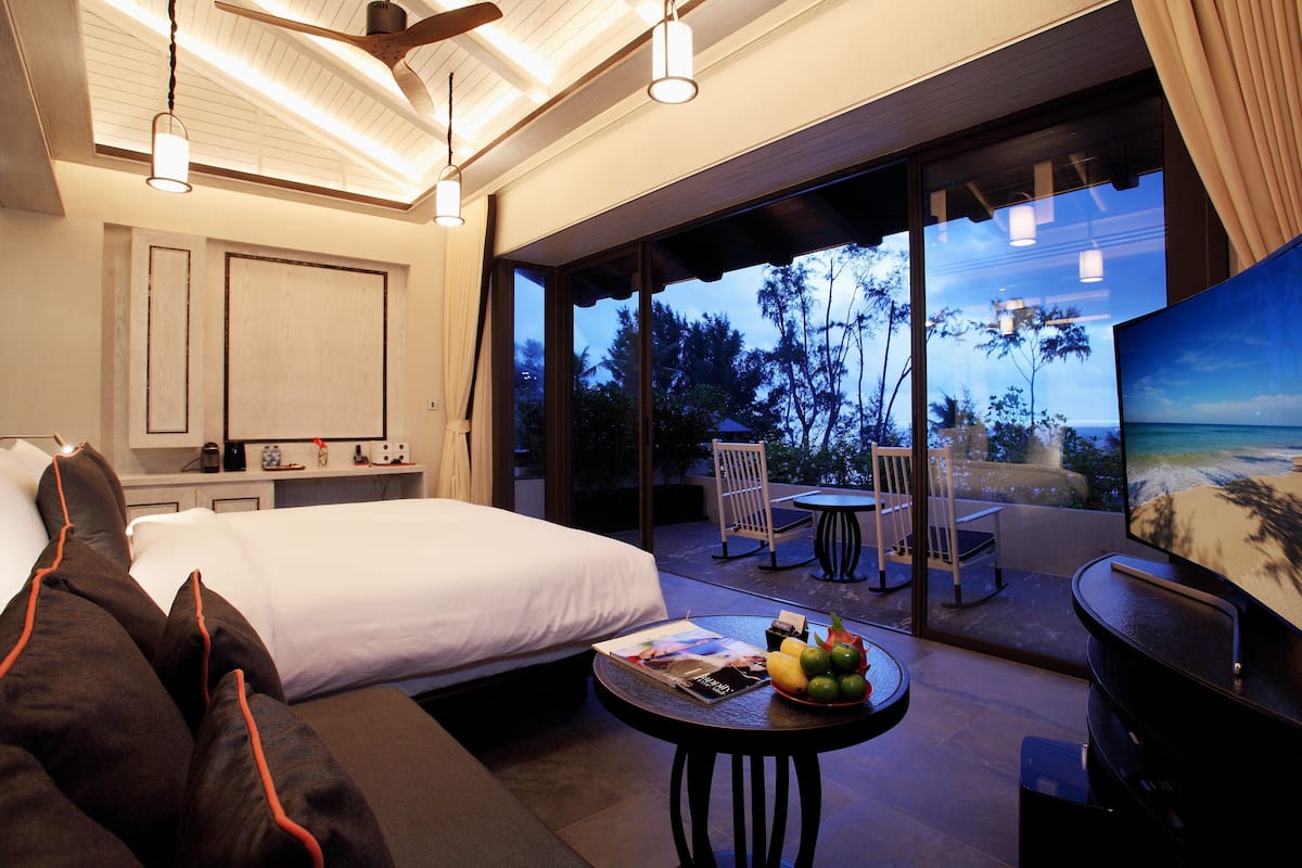 A bedroom with a bed, a small table with fruit, and a balcony with a table and chairs.
