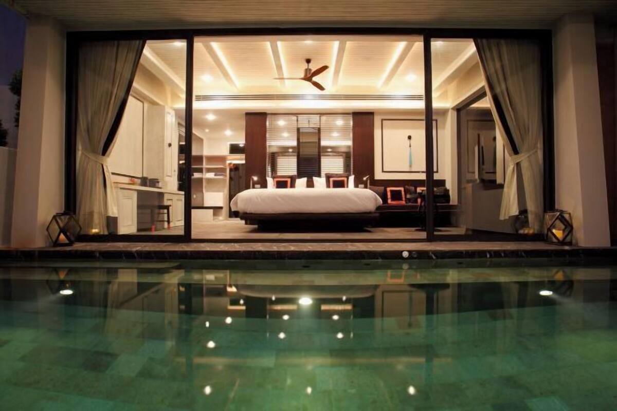 A modern hotel room with a large bed, a dining area, and a view of a swimming pool.