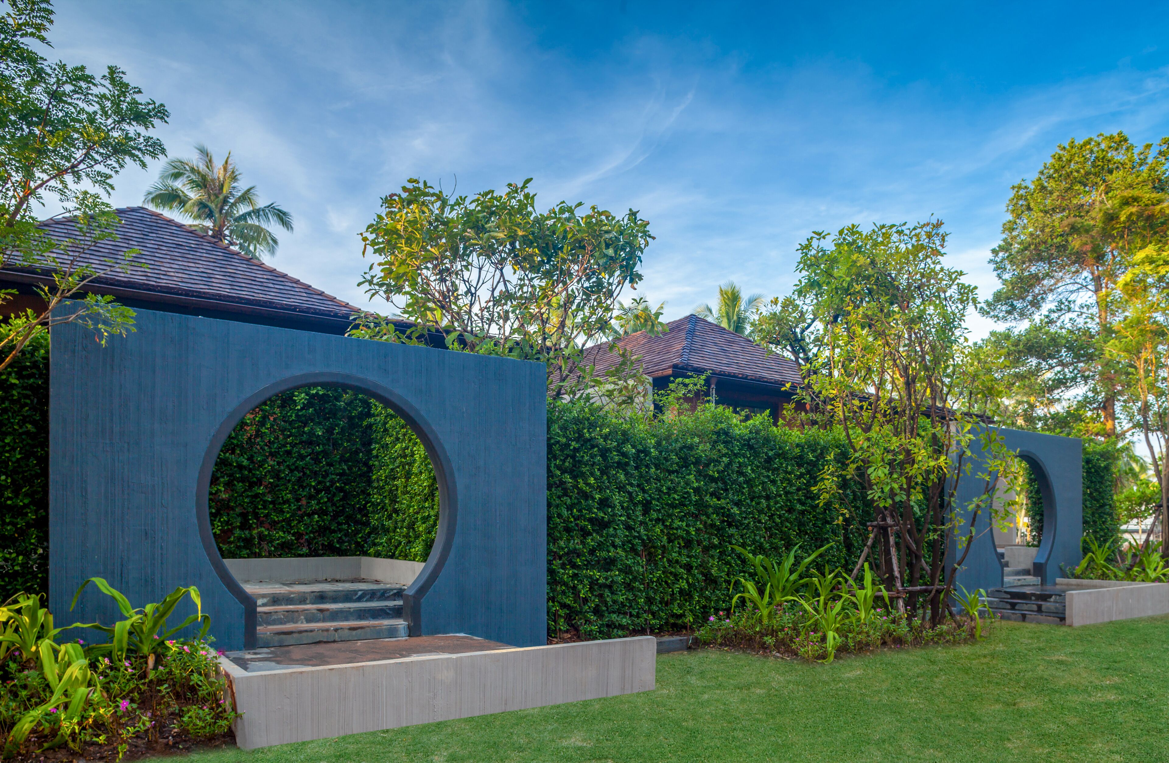 A modern building with a circular entrance, surrounded by lush greenery and palm trees.