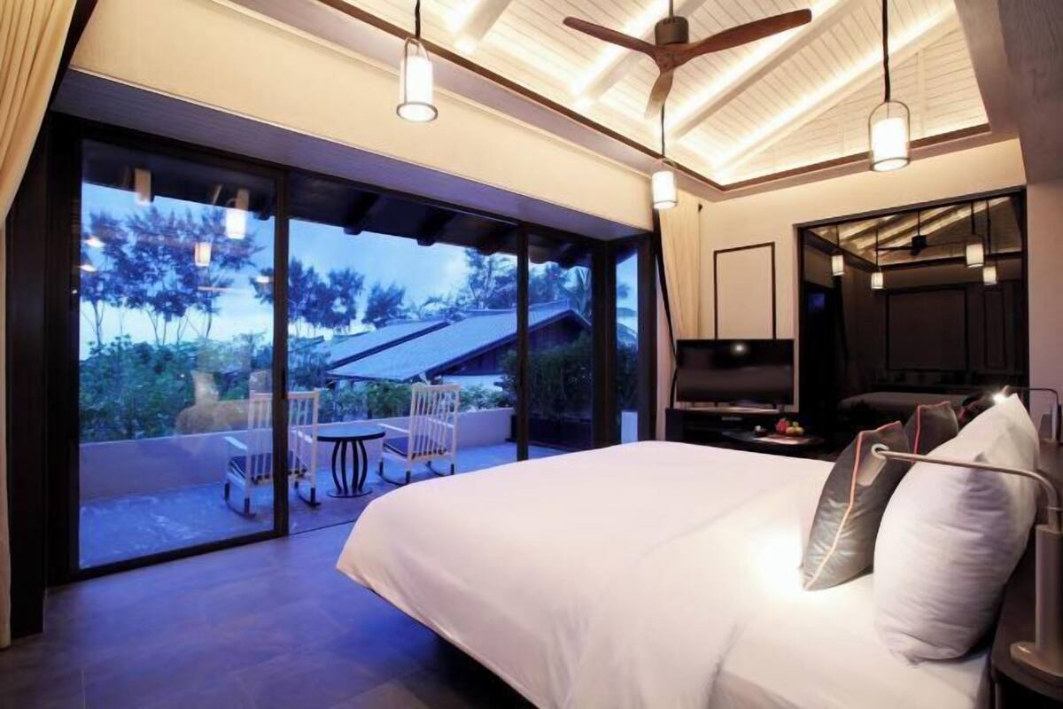 A modern bedroom with a large bed, a TV, and a balcony with a table and chairs.