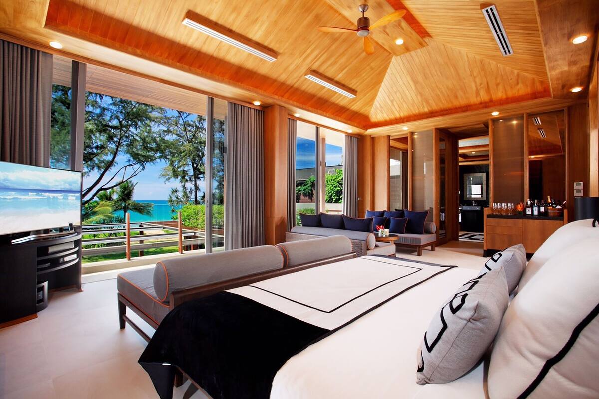A modern hotel room with a large bed, a TV, a seating area, and a view of the ocean.