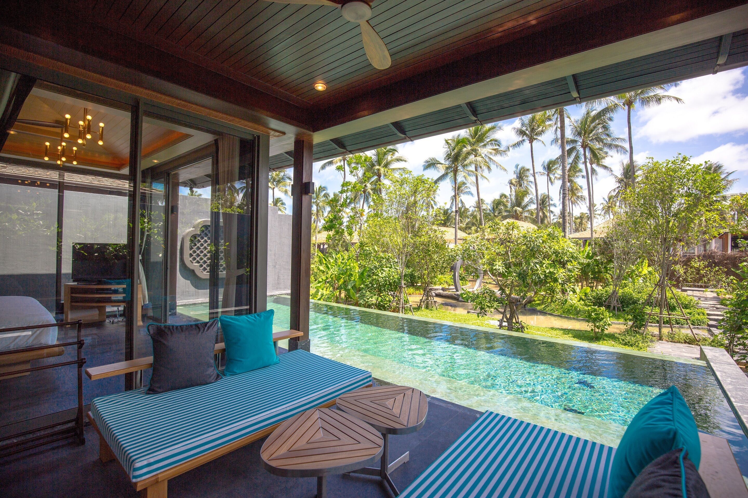 Un espacio lounge moderno al aire libre con piscina, asientos y vistas a palmeras.