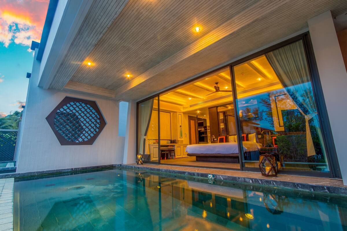 A modern hotel room with a large glass door leading to a balcony, a pool, and a view of the sky.