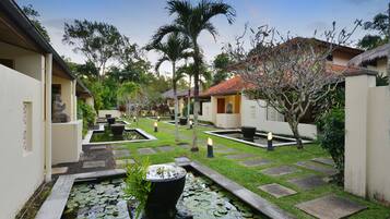 Surrounded by lush greenery and palm trees, this serene courtyard features a central water feature and a stone bench.