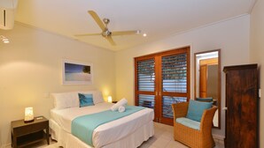 Ein Schlafzimmer mit einem Bett, einem Nachttisch, einem Sessel, einem Deckenventilator und einer Tür mit Glasfeldern.
