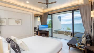 Habitación de hotel con una cama grande, un televisor sobre un soporte de madera, un balcón con vista al mar y un ventilador de techo.