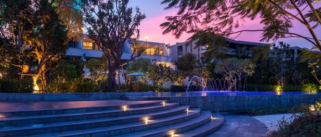 A modern hotel with a pool, outdoor stairs, and a sunset view.