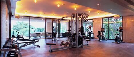 Ein geräumiges Fitnessstudio mit verschiedenen Trainingsgeräten, großen Fenstern und Holzboden.