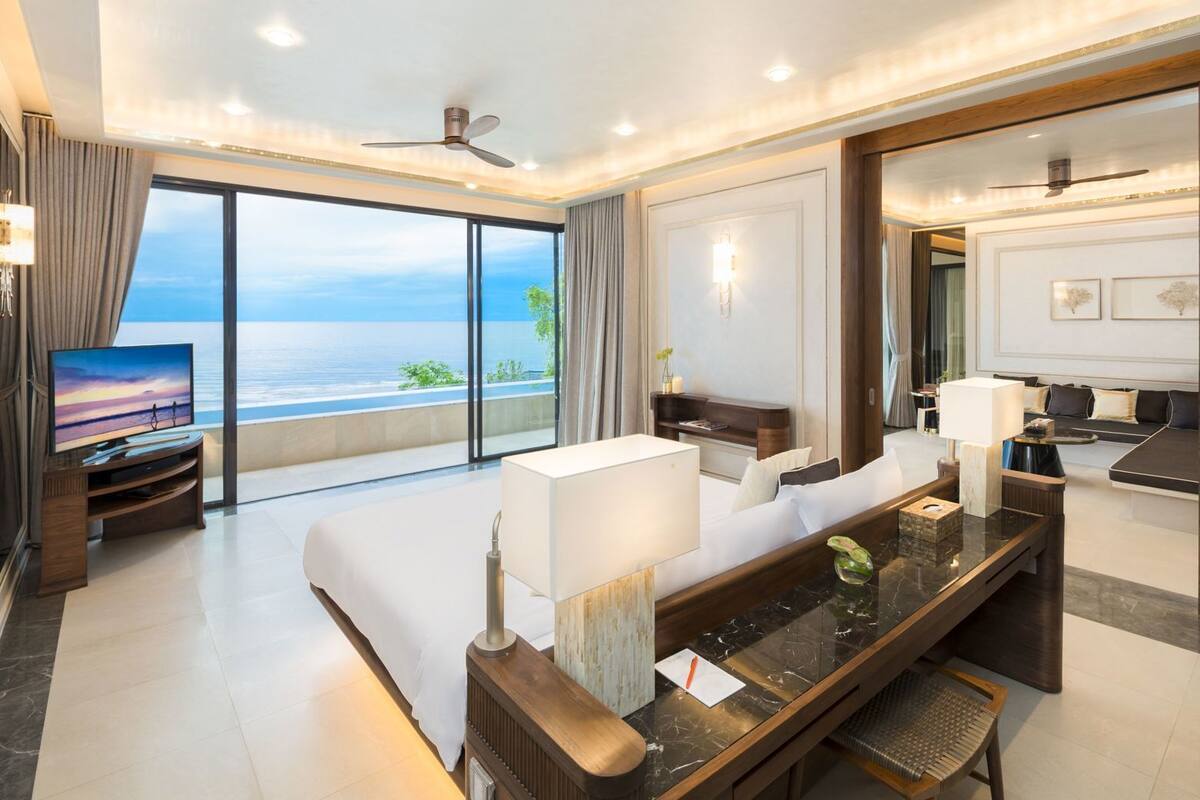Une chambre d’hôtel moderne dotée d’une grande fenêtre, d’un téléviseur à écran plat, d’un canapé, d’un coin repas et d’une salle de bain.