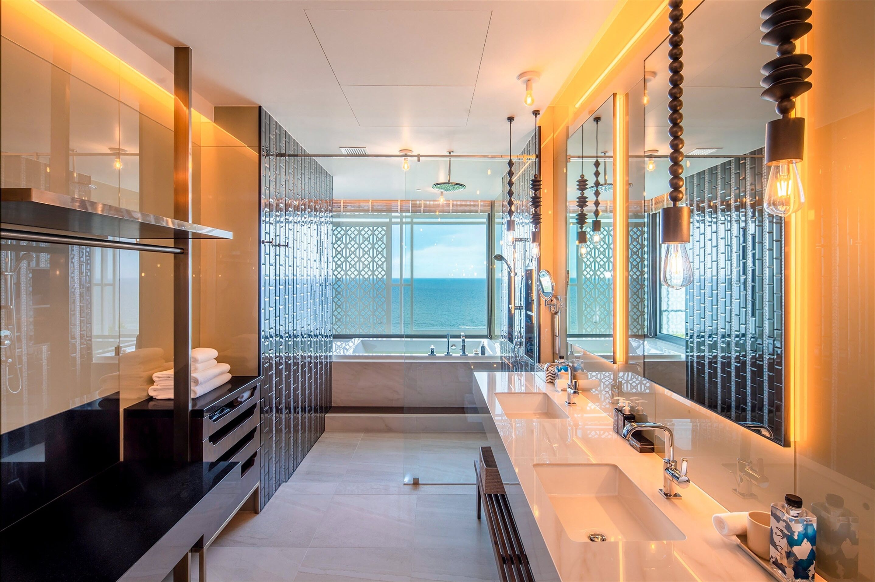 A modern bathroom with a large mirror, a sink, and a view of the sea.