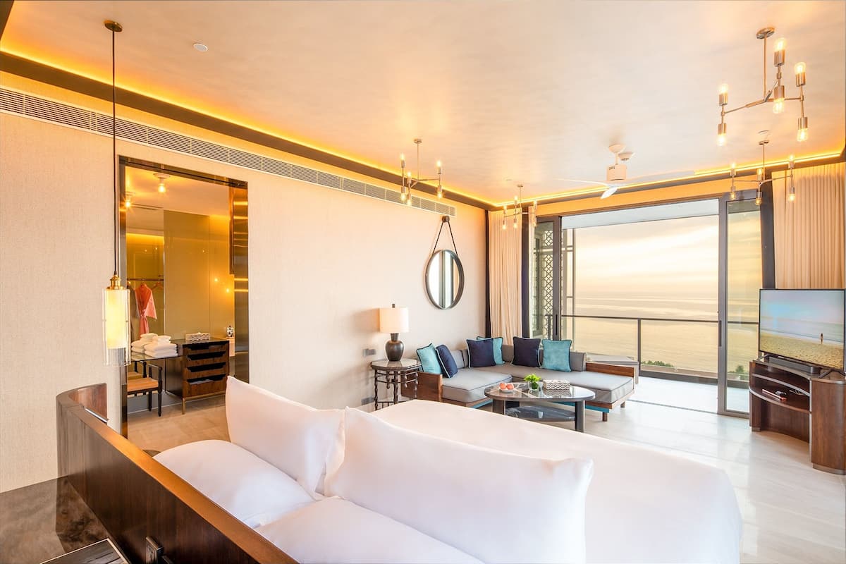 Une chambre d’hôtel moderne dotée d’un grand lit, d’un canapé, d’une télévision et d’un balcon offrant une vue sur la mer.