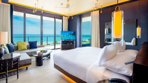 Quarto de hotel moderno com uma cama grande, uma televisão e varanda com vista para o mar.