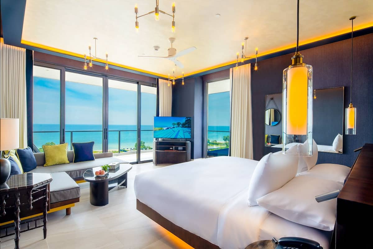 Une chambre d’hôtel moderne dotée d’un grand lit, d’une télévision et d’un balcon offrant une vue sur l’océan.