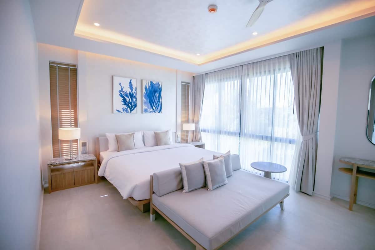 Une chambre d’hôtel moderne avec un grand lit, des tables de chevet, une table ronde et une grande fenêtre avec des rideaux.