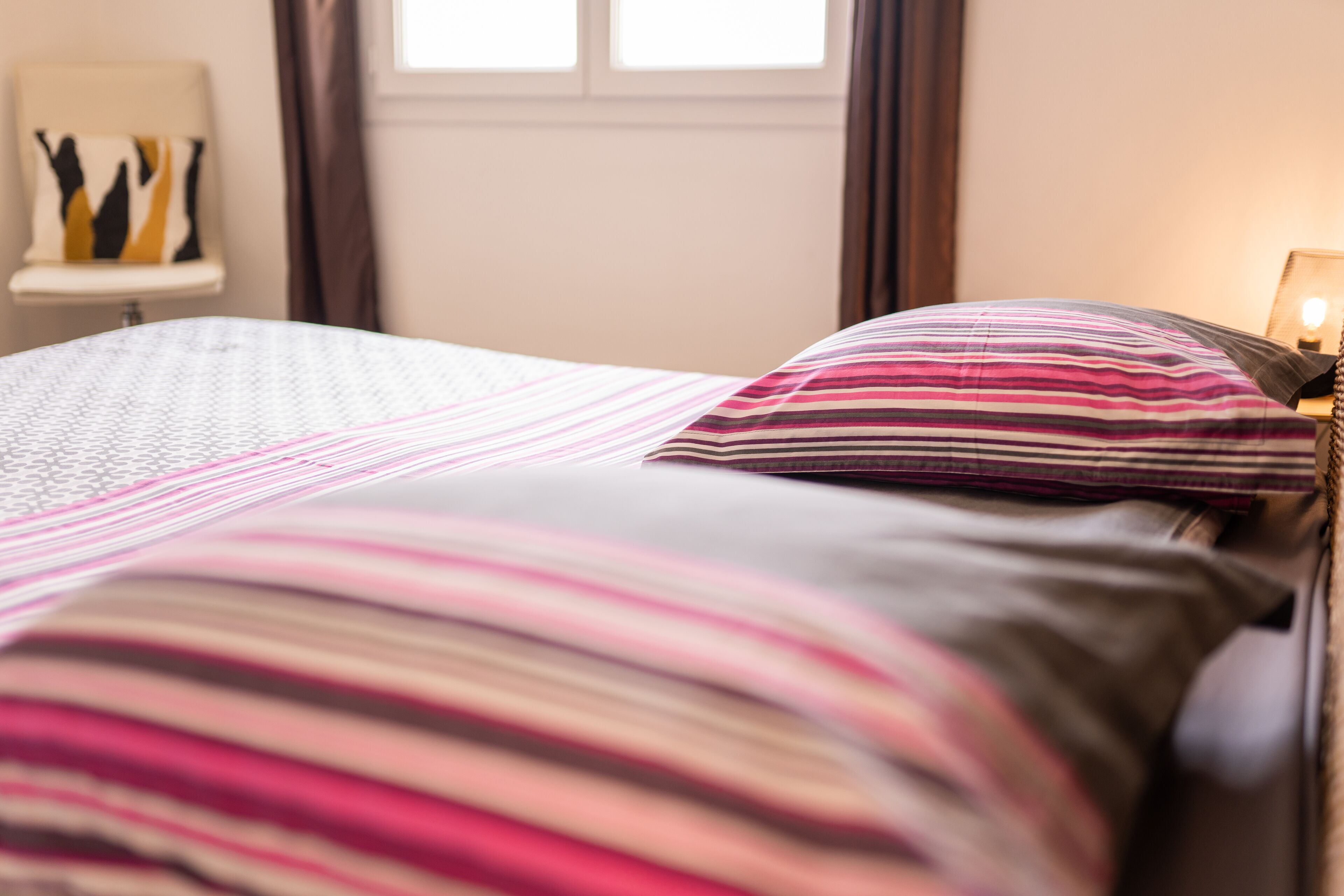 A bed with striped bedding and a bedside table with a lamp.
