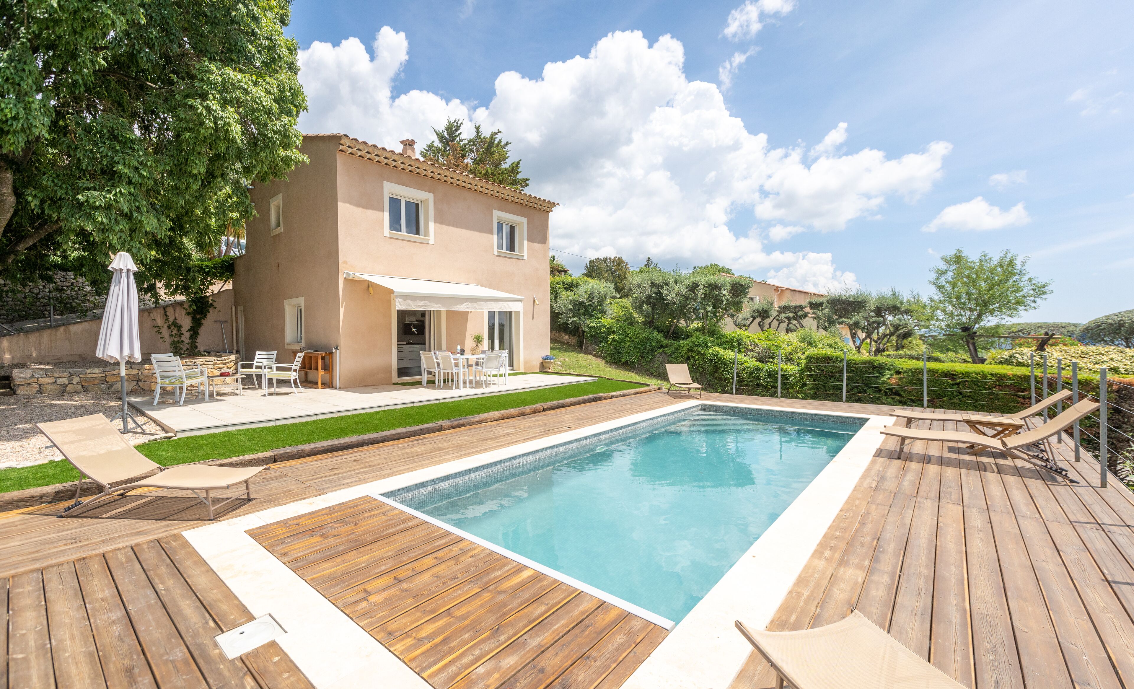 A poolside area with a wooden deck, a pool, and a house with a patio.
