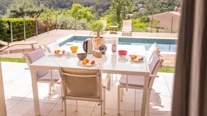 Una taula de menjador amb caires i vista a una piscina i les colines al fons.