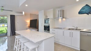 Eine moderne Küche mit weißen Schränken, einer großen Kochinsel mit Barhocker, einer eingebauten Mikrowelle, einem Backofen und einem Geschirrspüler sowie einem Wandgemälde mit Fischmotiven.