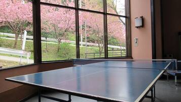 A ping pong table in a room with large windows overlooking a garden with pink blossoms.