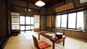 A traditional Japanese room with tatami flooring, a low table with cushions, and sliding doors. - Hinoderyokan (Ise)