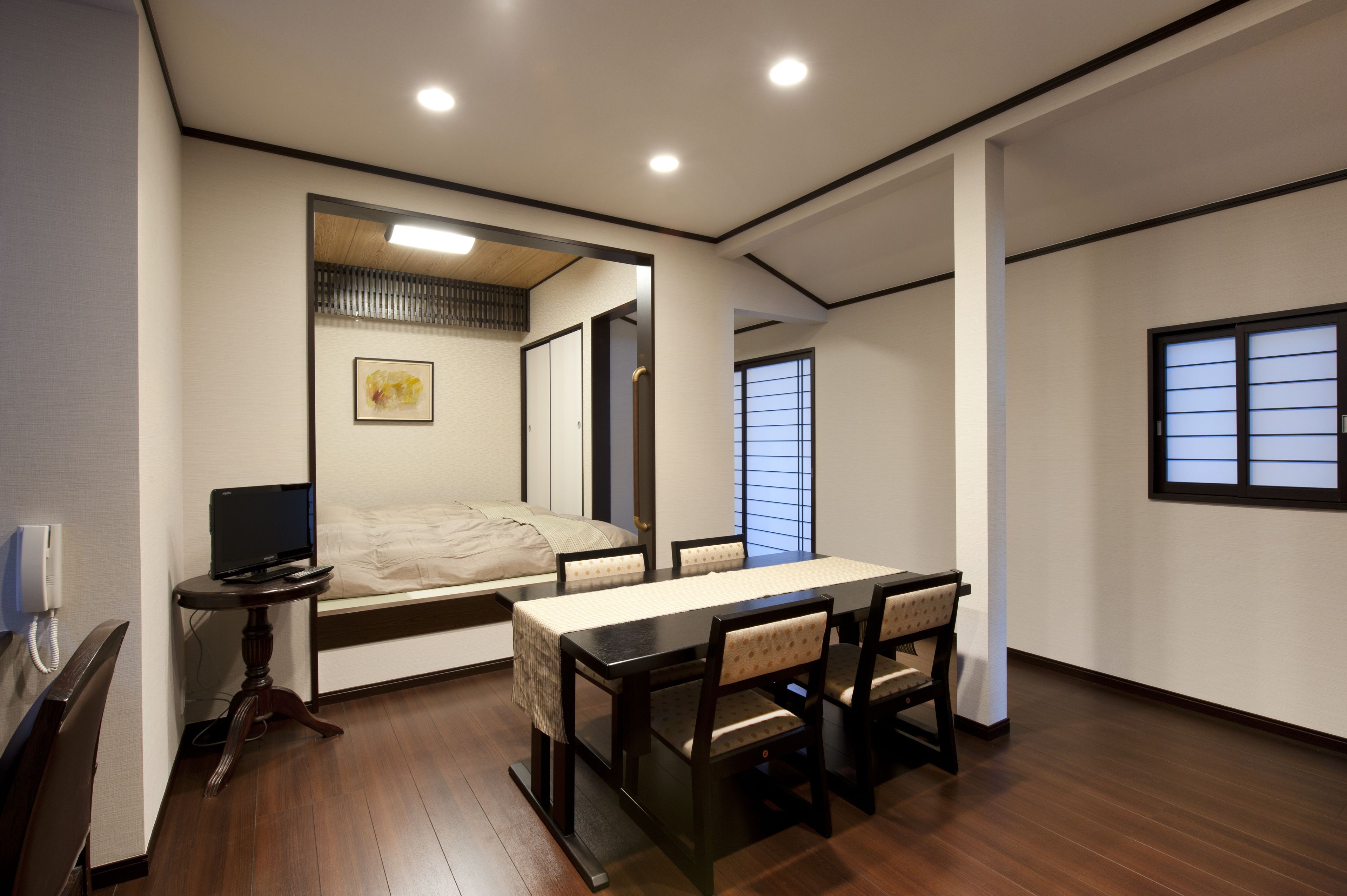 Una habitación con una cama, una mesa de comedor con sillas, una mesita auxiliar y una ventana con persianas.