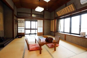 Una habitación japonesa tradicional con suelo de tatami, una mesa baja con cojines y un puertas correderas que dan a otra habitación.