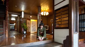 A traditional Japanese interior with wooden floors, a staircase, and a person in a kimono. - Hinoderyokan (Ise)