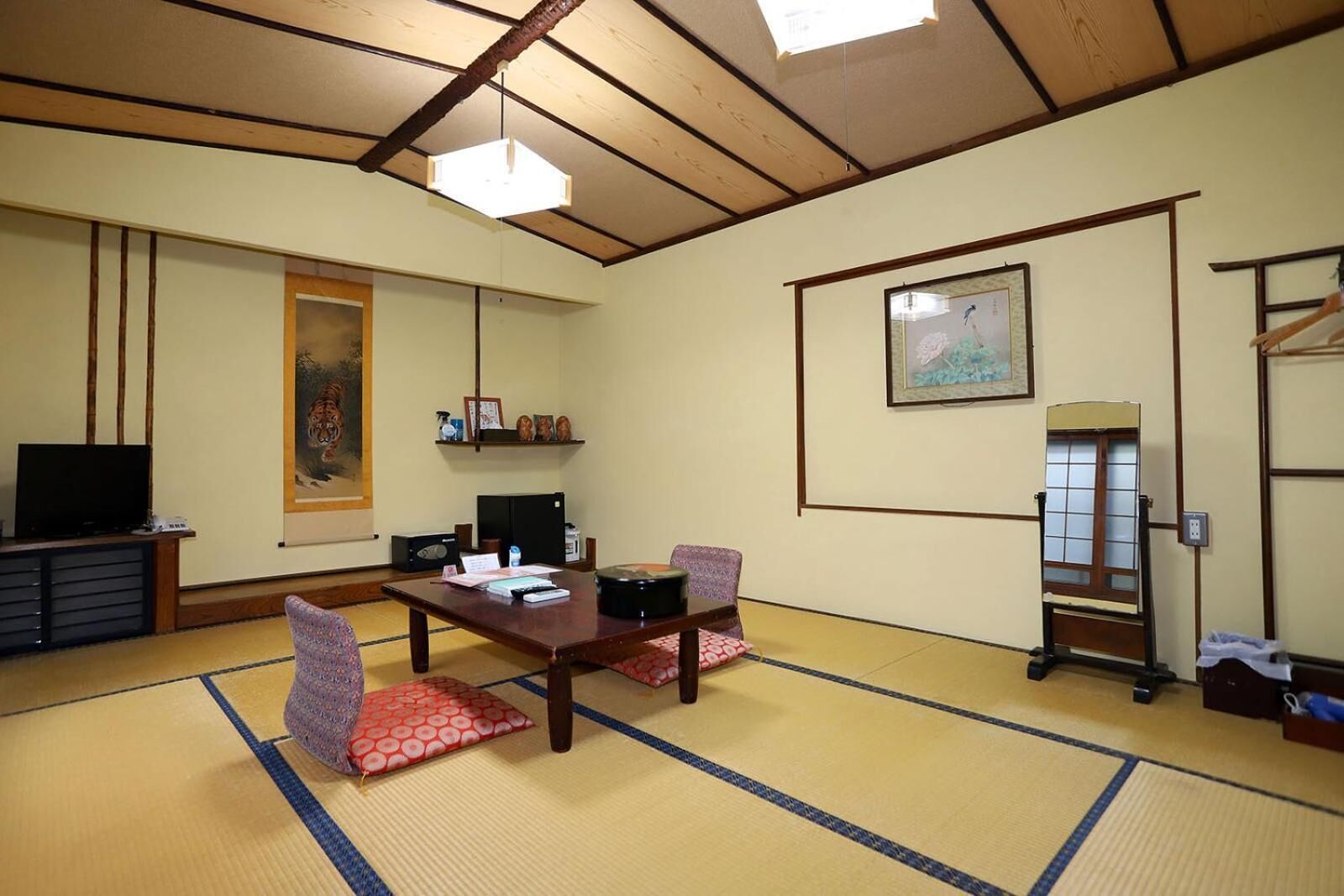 A traditional Japanese room with tatami flooring, a low table with cushions, a television, and artwork on the walls.