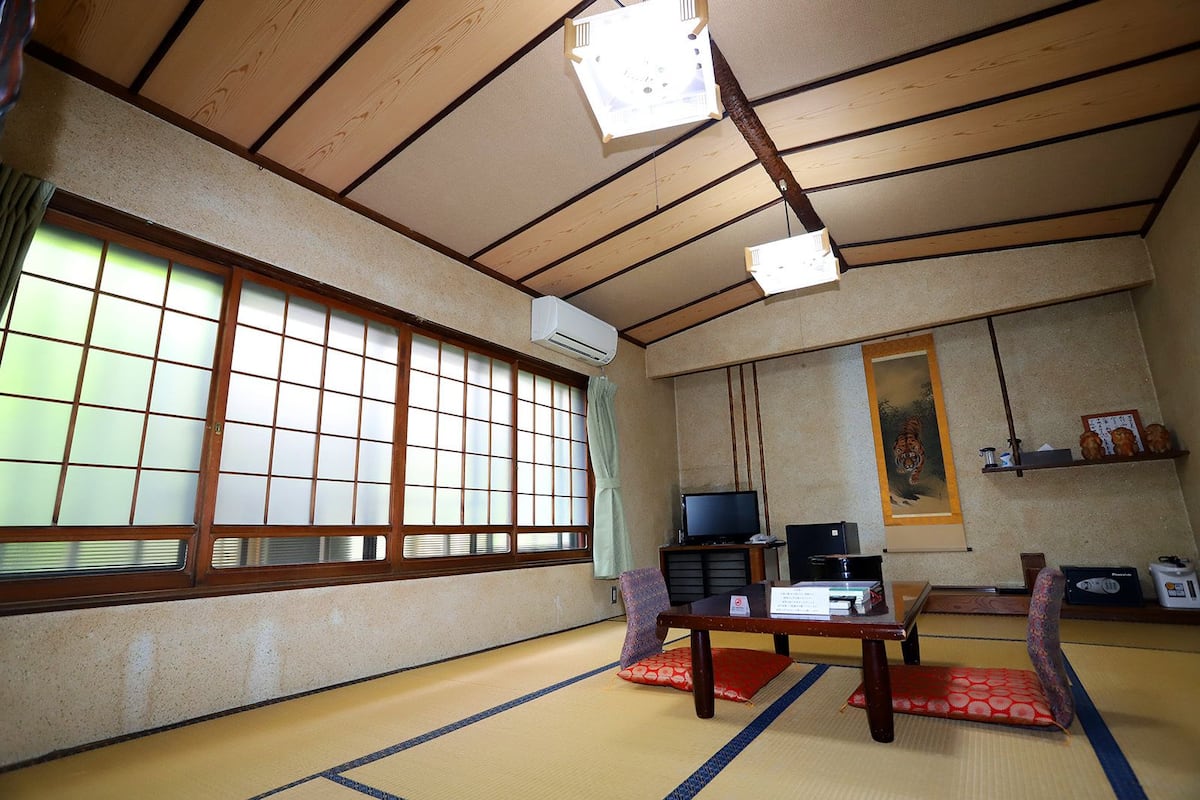 A traditional Japanese room with tatami flooring, a television, a desk, and a painting on the wall.