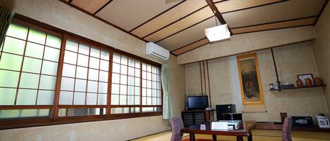 A traditional Japanese room with tatami flooring, a television, a desk, and a painting on the wall.