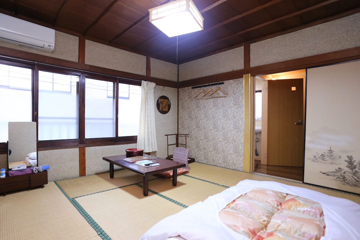 A traditional Japanese room with tatami flooring, a futon bed, a wooden table, and a shoji screen door.