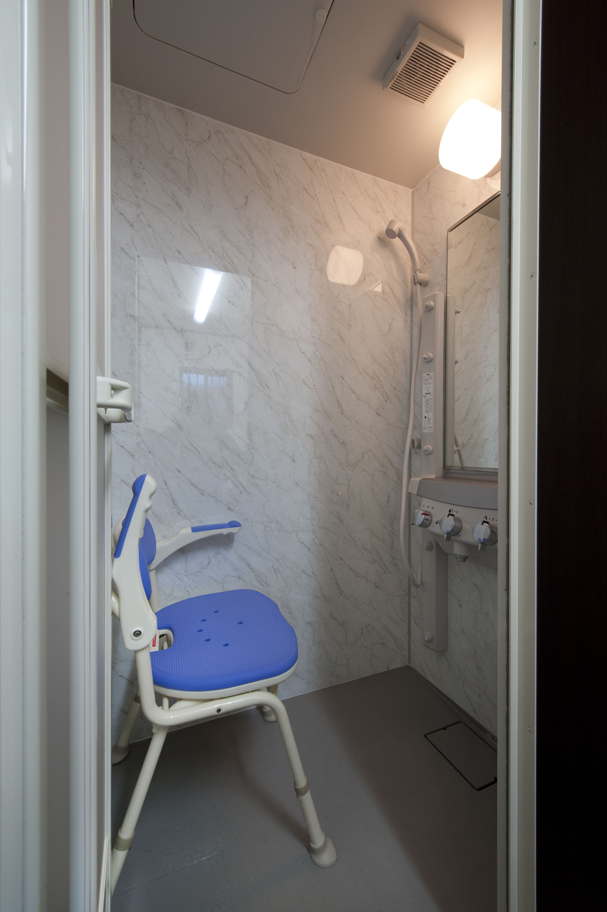 A bathroom with a shower, a white toilet, and a blue chair.