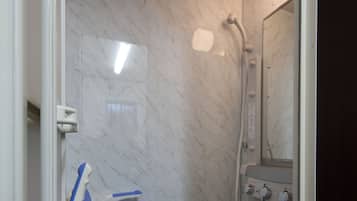 A bathroom with a shower, a white toilet, and a blue chair.