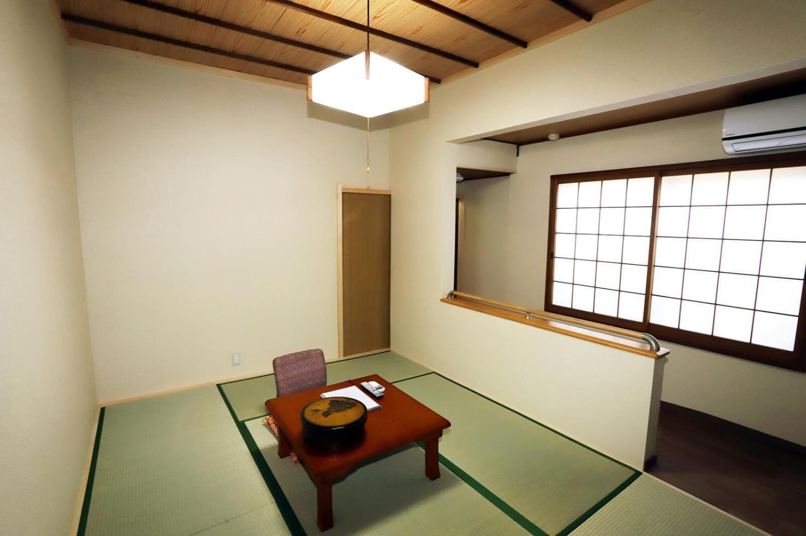 A traditional Japanese room with tatami flooring, a low wooden table, a chair, and a shoji screen window.