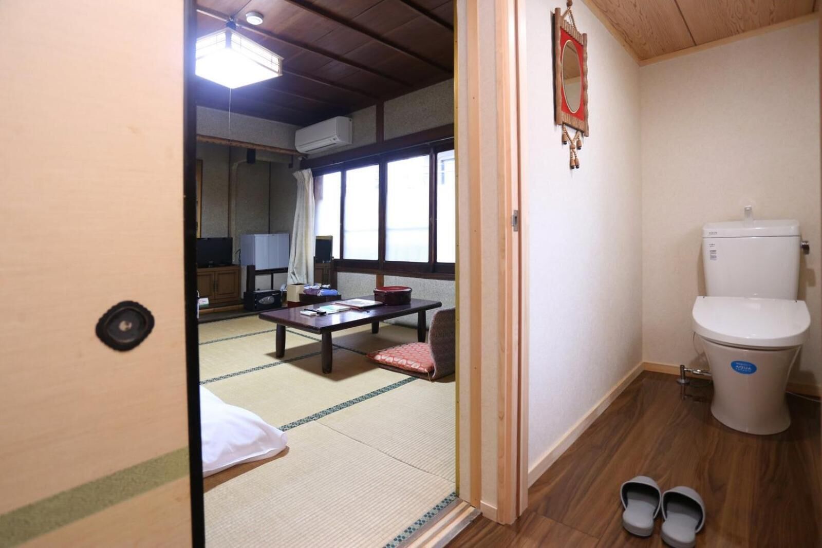A traditional Japanese room with tatami flooring, a tatami mat table, a low wooden desk, a toilet, and a sliding door leading to another room.
