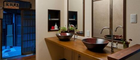 Un baño con piso de madera, dos lavamanos con espejos grandes y un mueble de tocador de madera.