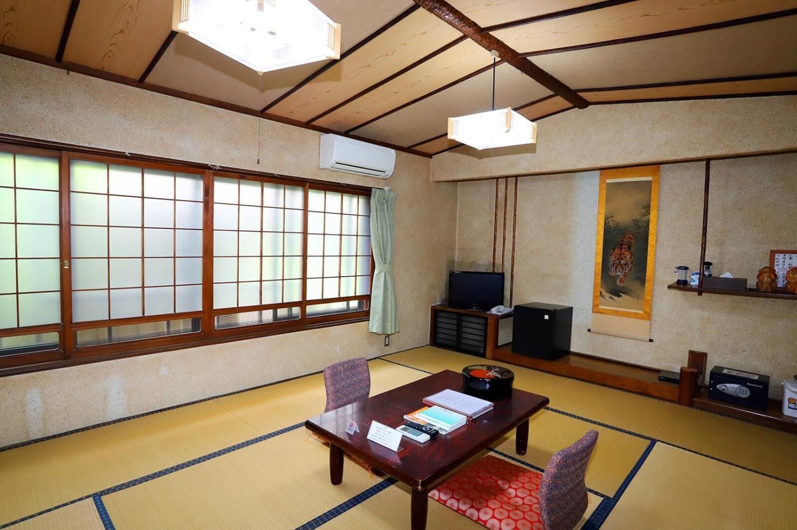 Ein traditioneller japanischer Raum mit Tatami-Boden, einem niedrigen Tisch mit Kissen, einem Fernseher und einem Tigerbild.