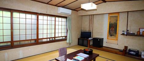 Ein traditioneller japanischer Raum mit Tatami-Boden, einem niedrigen Tisch mit Kissen, einem Fernseher und einem Tigerbild.