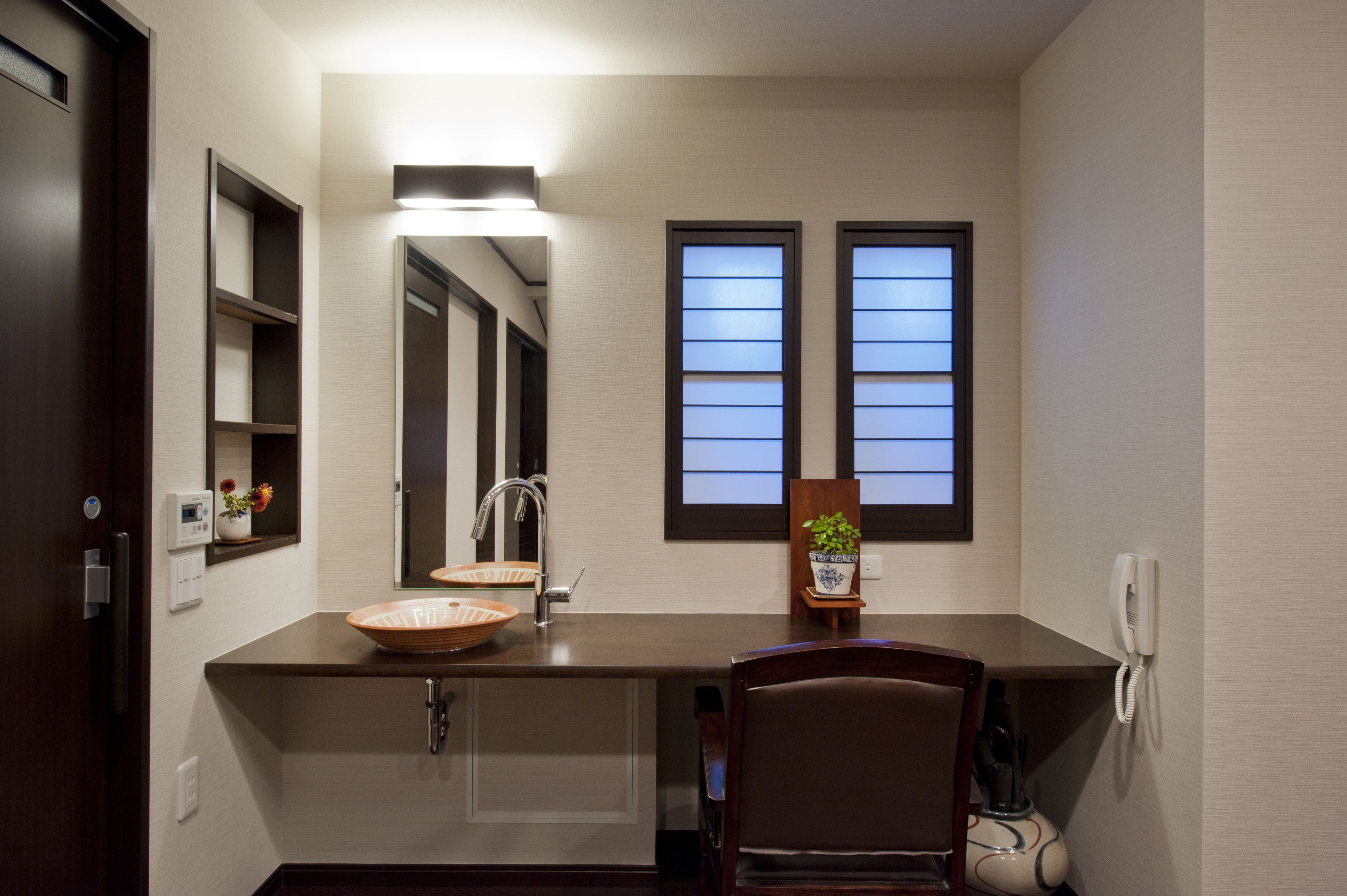 A modern bathroom with a large mirror, two windows, a sink, and a chair.