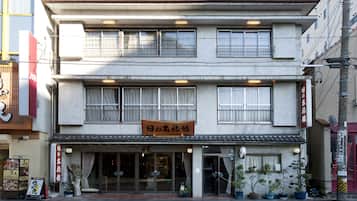 Traditional building with a tiled roof and metal grilles, featuring a glass entrance and potted plants.