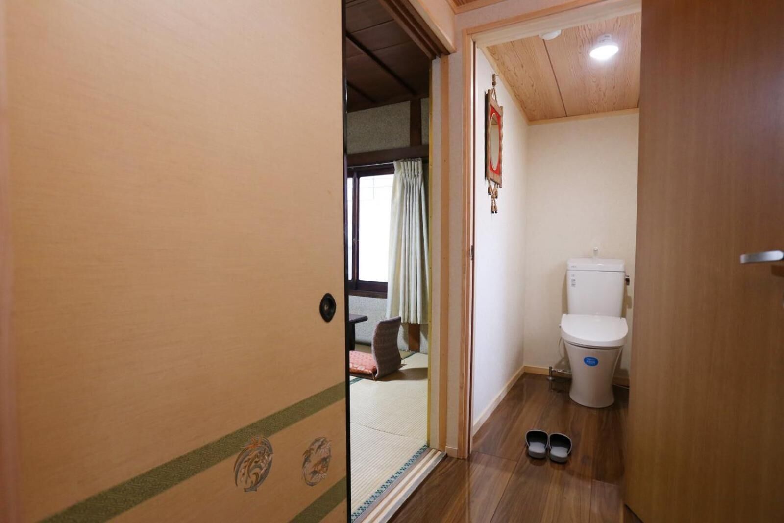 A small, compact bathroom with a toilet, a mirror, and a pair of shoes on the floor.