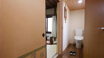 A small, compact bathroom with a toilet, a mirror, and a pair of shoes on the floor.