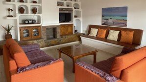 Un salon avec une cheminée, des canapés orange, une table basse et un téléviseur.