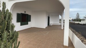 Un espace extérieur abrité avec un sol carrelé, un bâtiment blanc avec une porte, et un camion Toyota garé.