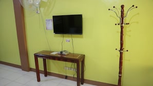 A room with a wooden table, a television mounted on the wall, and a coat rack. - Centillo Travellers Inn (Malay)