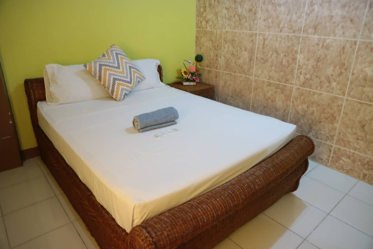 A neatly made bed with a white mattress, a brown woven headboard, and a decorative pillow.