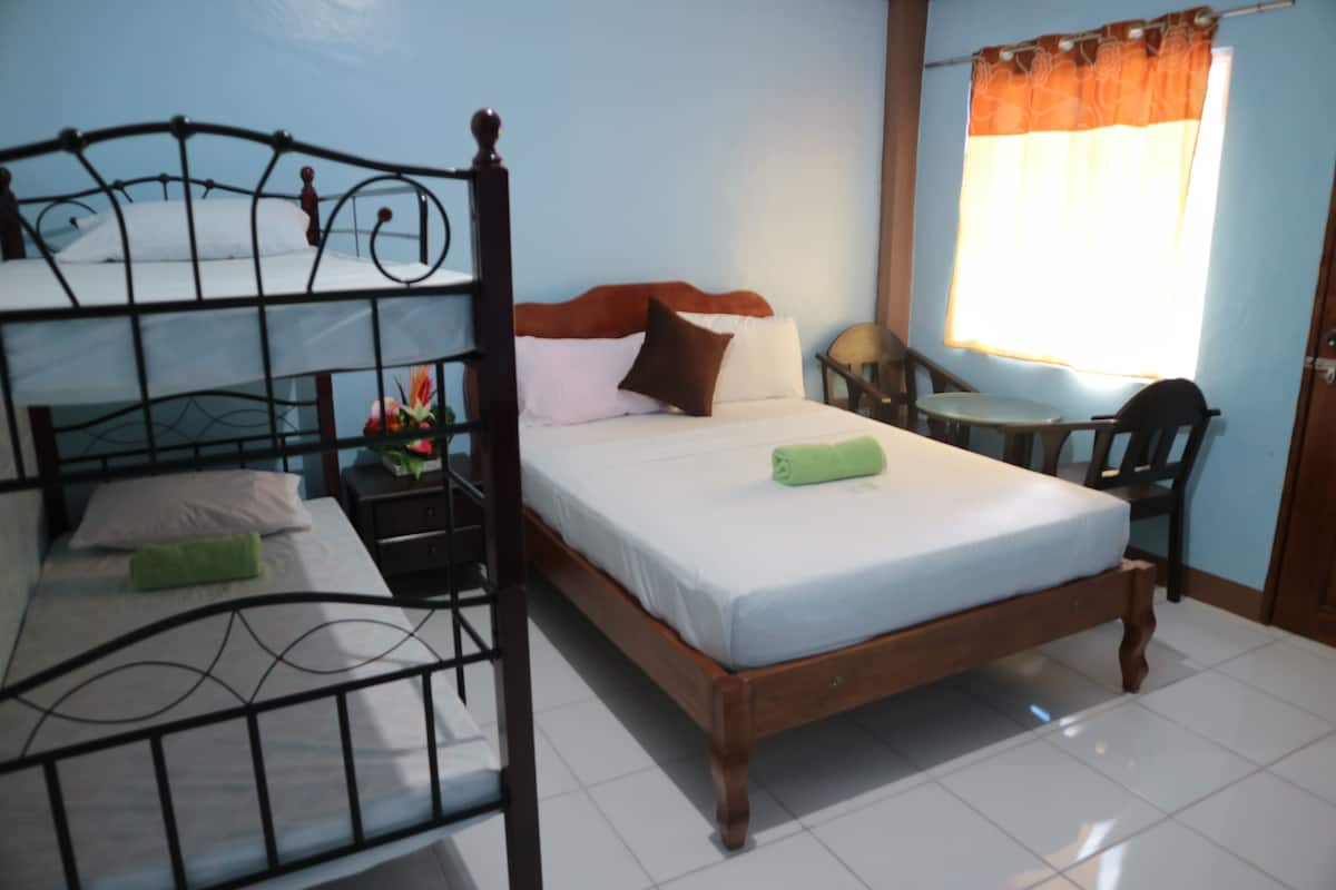 A room with a bunk bed, a single bed, a nightstand with a lamp, and a window with curtains.